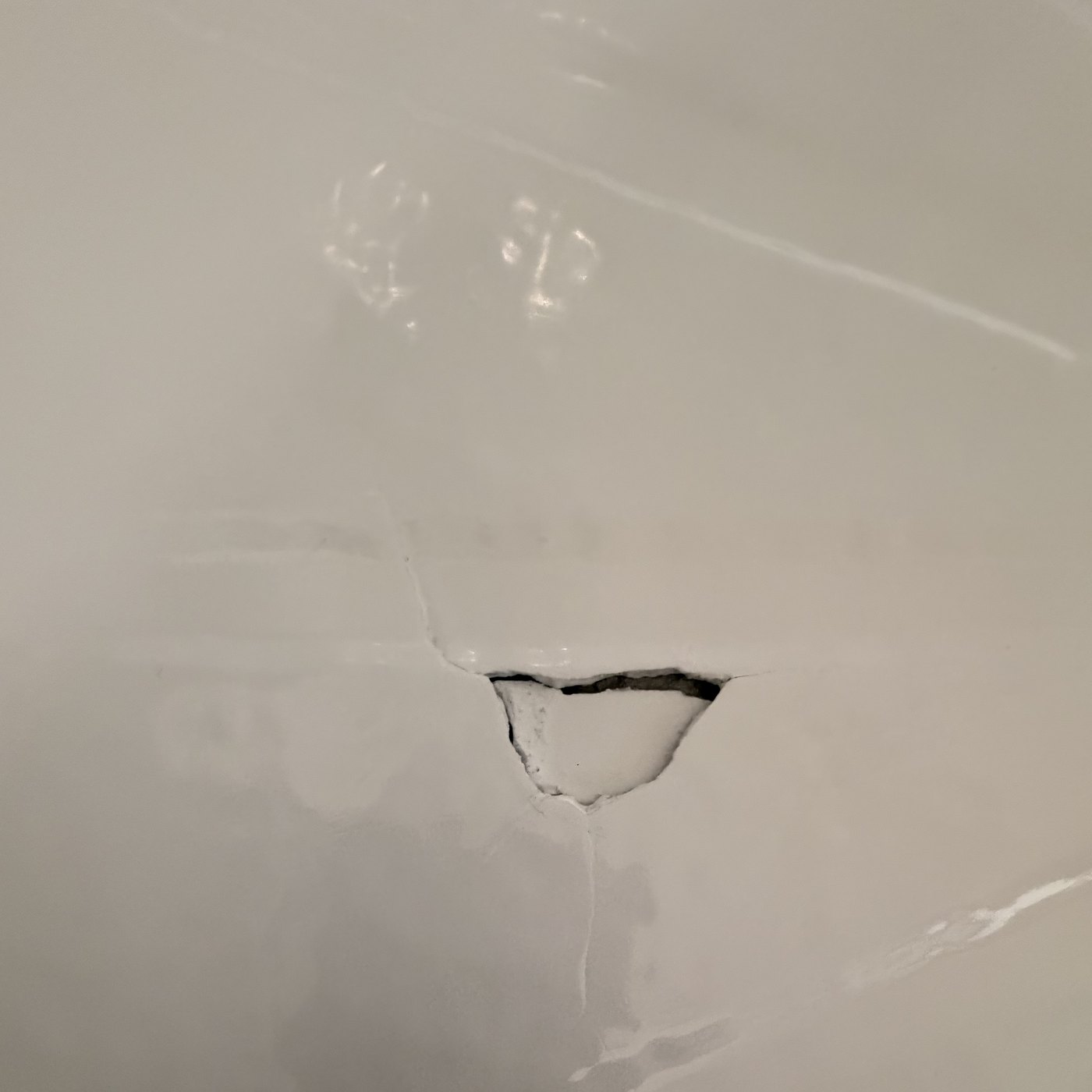 Before — a cracked fiberglass shower pan with two holes broken through the floor.